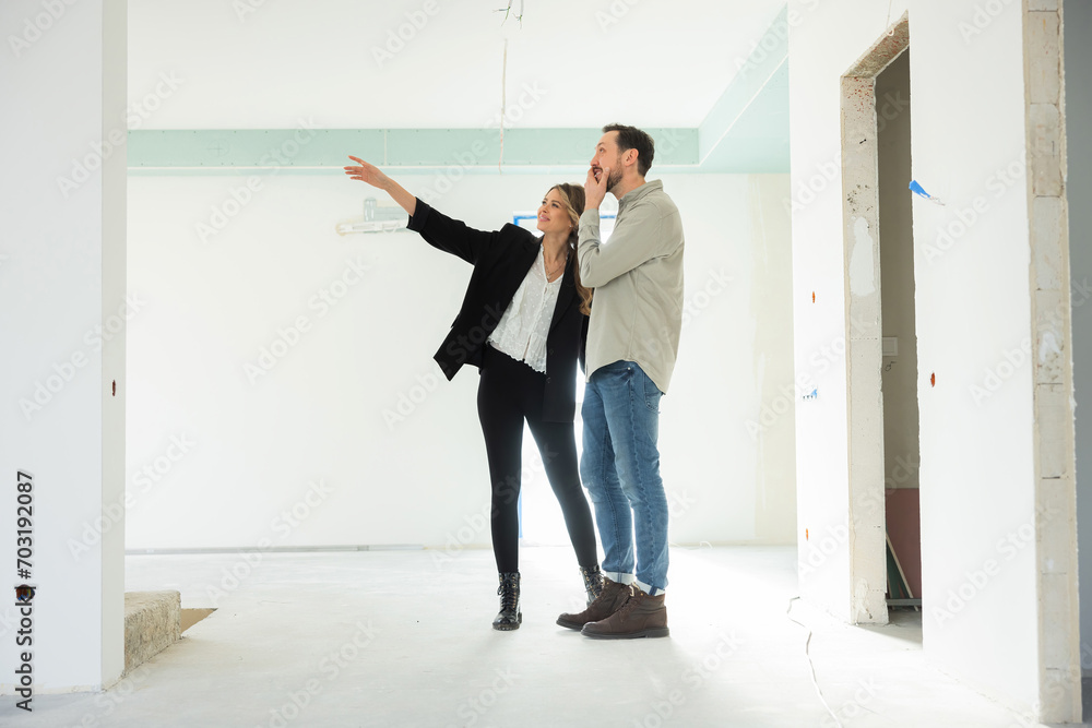 Fototapeta premium Happy ownerships owners of a new house delighted wife and husband observing examining new house discussing all furniture.