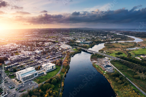 Aerial view on Galway city suburbs and river Corrib at sunset. Dramatic rich cloudy sky. Town high populated area. Irish landscape view.
