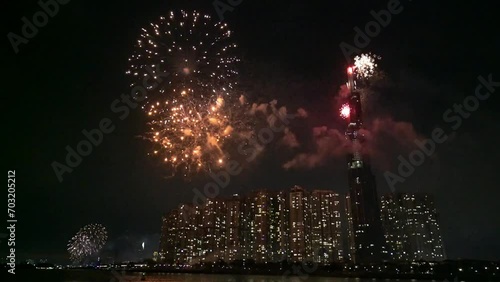 Colorful fireworks in the sky glowing at night beside the skyscraper in the riverside urban area welcoming the lunar new year in Vietnam