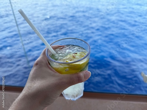 Enjoying a cold iced non-alcoholic mojito in a glas with plastic straw on a cruise ship with the ocean in the background