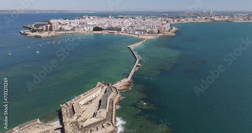 Aerial drone cityscape view of Cádiz in Spain, Andalusia, Europe, on bright sunny day, facing La Caleta beach and city waterfront. Drone slowly flying backwards. Shot in 5K ProRes 422 HQ photo