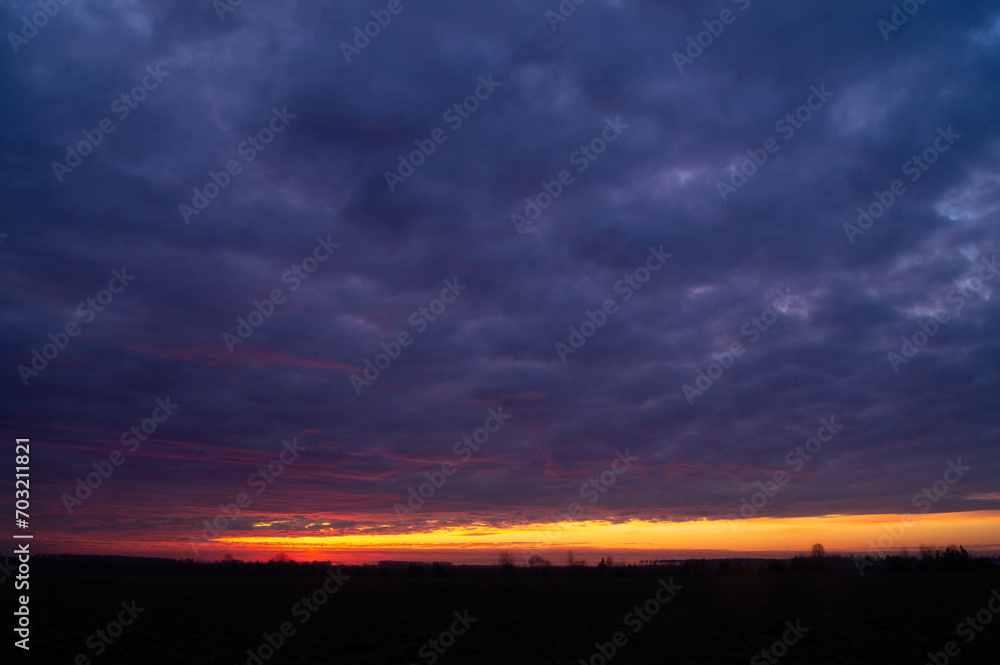 Dramatic December sunrise over Ukrainian fields, where the sky ignites with fiery streaks. Winter dawn's palette stretches across the early morning sky, awash with vibrant colors.