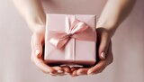 Close up shot of female hands holding a small gift wrapped with pink ribbon. Generative AI.