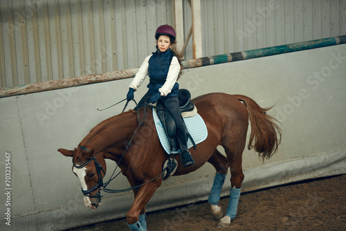 Concentrated little girl in inform and special clothes siting on horse, training horseback riding on special manege. Concept of sport, childhood, school, course, active lifestyle, hobby