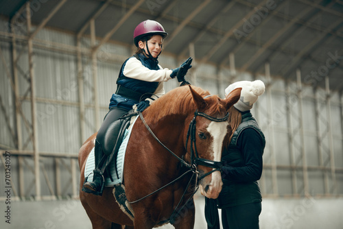Good lesson,. Little girl giving high five to her instructor. Learning horseback riding on special arena. Concept of sport, childhood, school, course, active lifestyle, hobby © master1305