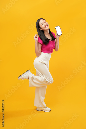 full-body portrait of an happy Asian woman holding a cell phone on a yellow background