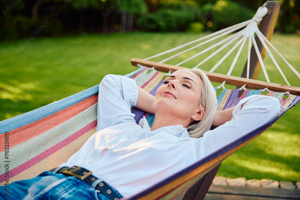 Beautiful mature woman lying in hammock in her house backyard. Staycation concept. Beautiful mature woman lying in hammock in her house backyard. Staycation concept.