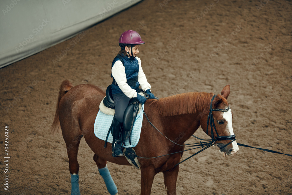 Top view. Child, little girl on training course, lesson, learning, practicing horseback riding. Concept of sport, childhood, school, course and active lifestyle, hobby Top view. Child, little girl on training course, lesson, learning, practicing horseback riding. Concept of sport, childhood, school, course and active lifestyle, hobby
