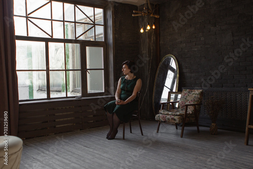 an adult woman sits thoughtfully on a chair, sofa. woman dreams, sits in dark interior © Yevgeniya