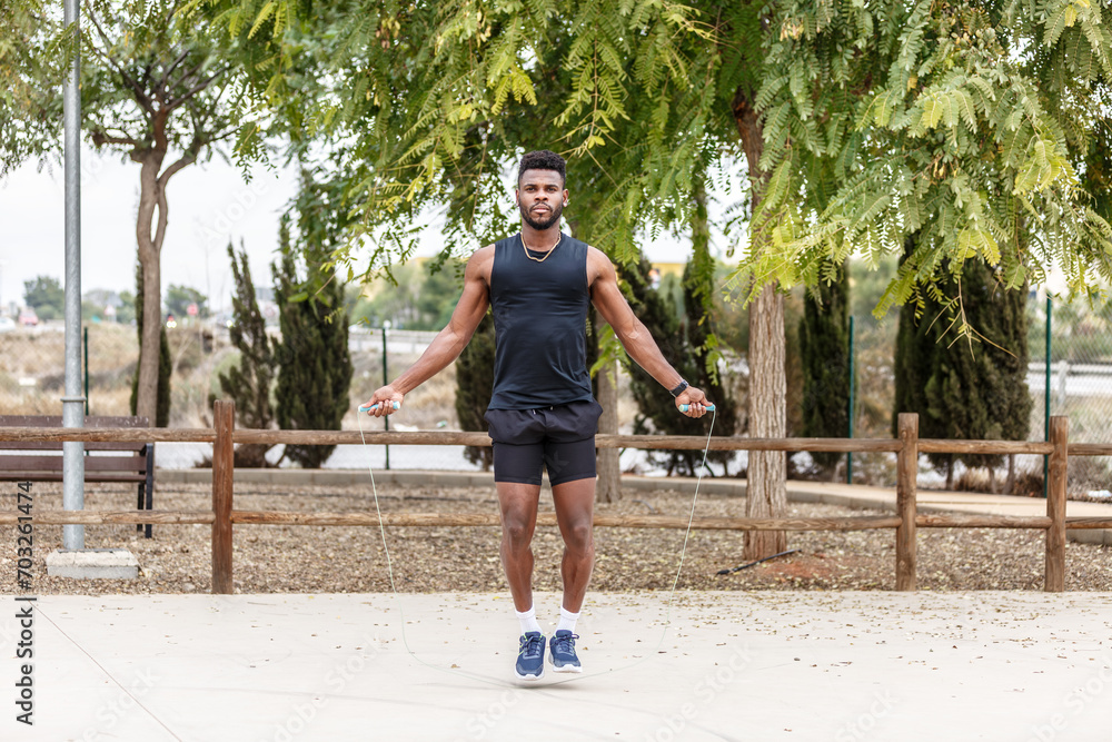 Fototapeta premium Strong sportsman jumping rope against green trees