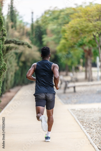 Anonymous African American sportsman running along park during fitness training