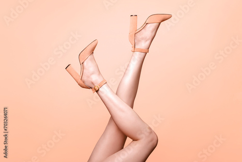 Sexy woman's female smooth legs in trendy fuzz peach 2024 pantone color of the year high heels shoes isolated on peach background, footwear and depilation advertising banner in monochrome colors photo