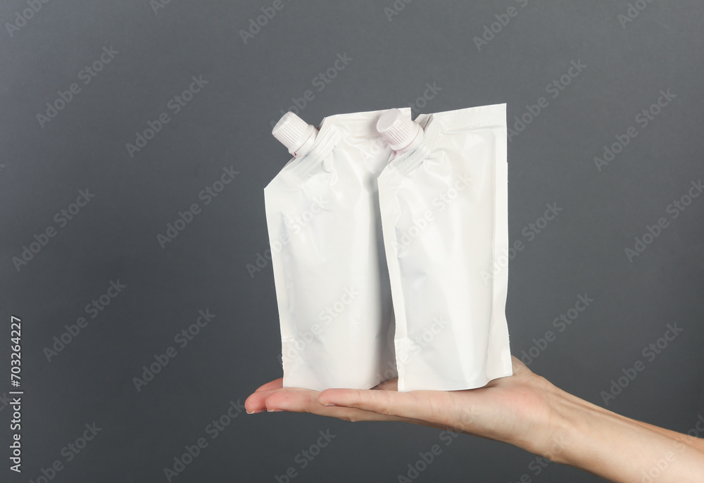 White doy packs with dispensers on hand palm, dark gray background. Template for design, mockup White doy packs with dispensers on hand palm, dark gray background. Template for design, mockup