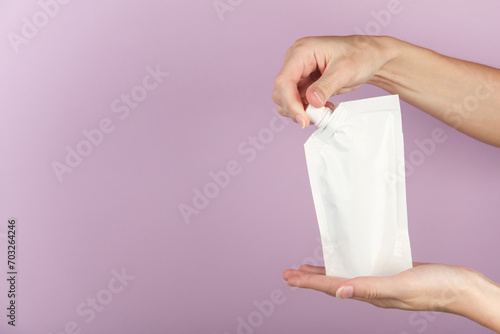 фотографія Hands open white doy pack with dispenser on dark gray background