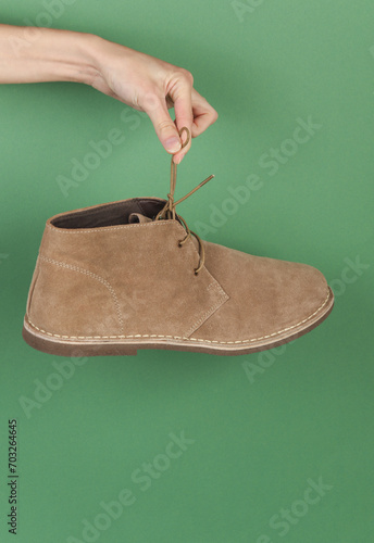 Hand holds suede desert boot by the lace on a green backgroun photo