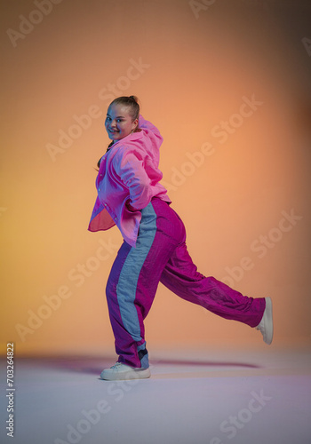 Energetic young woman in pink clothes dancing to the rhythms of jazz funk against the background of a studio with orange light. The photo is perfect for the concepts of freedom of expression.