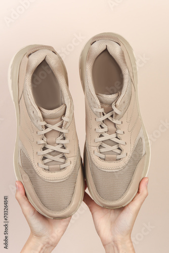 Female hands holding sports sneakers on a beige background