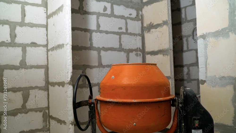 Mixing cement mortar, laying bricks. Repairing the floor in an apartment using a concrete mixer. An orange concrete mixer in an apartment during an apartment renovation.