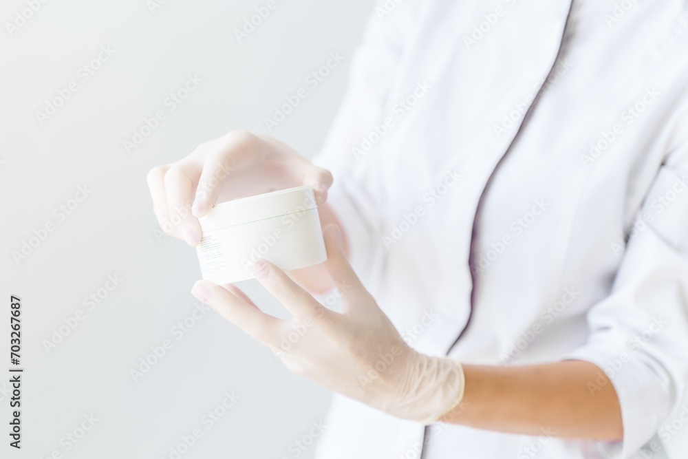 A cosmetologist in disposable gloves opens a face cream. Concept cosmetology, hygiene, facial care, dermatology A cosmetologist in disposable gloves opens a face cream. Concept cosmetology, hygiene, facial care, dermatology