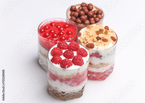 Homemade layered Desserts in a glass cups with yogurt, berries, cookie and chocolate balls on white background