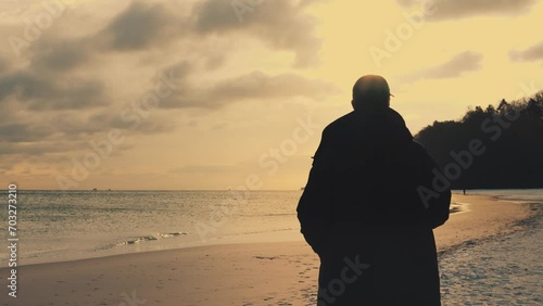 Young male in coat standing  and looking at the horizon with during the bright sunset. Concept of solitude to non tourist spots places.