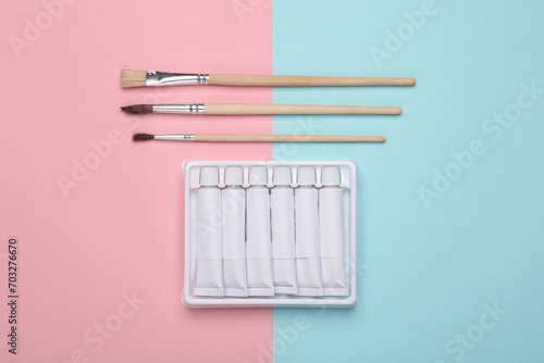Set of white empty tubes of acrylic or oil paint and brushes for creativity on pink blue background. Template for design  mockup