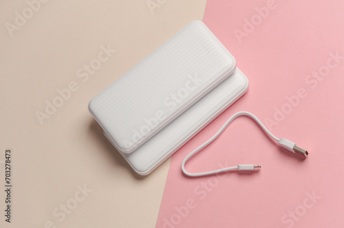 White power banks with cable on pastel background. External batteries for charging smartphone and other gadgets. Top view