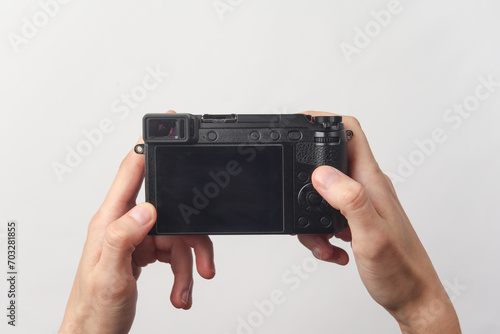 Hands holding a modern mirrorless camera with the screen facing up on white background