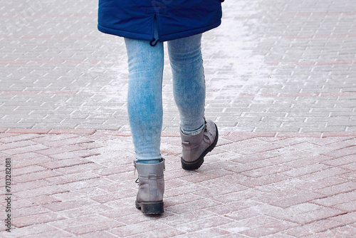 Woman walking on salted sidewalk. Salt sprinkled on paving slabs, prevention of pedestrian injury. Female feet in winter boots walking on salted pavement. Treating roads with salt in winter