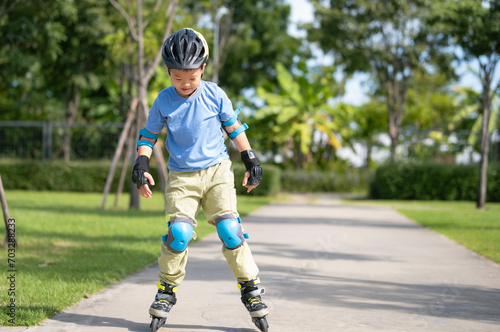 Cute little smiling Asian 7 years old child rollerblading in protection, helmet in sunny summer day, Young inline skater at the park, Child roller skating, Active sport kids on nature.