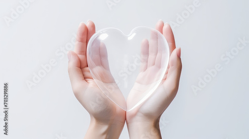 Hands holding glass transparent heart isolated on flat white background with copy space for text, banner template. Valentine's Day, charity, love and care.