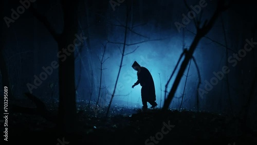 Mysterious dark figure in the night foggy forest. Silhouette of an unrecognizable man in a tunic with a hood. photo