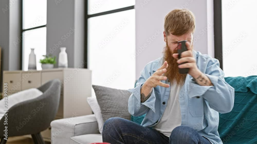Irish redhead man, sitting in the living room, stressed about his conversation on his smartphone, fighting with frustration and despair Irish redhead man, sitting in the living room, stressed about his conversation on his smartphone, fighting with frustration and despair
