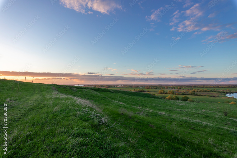bright blue sky with sunset clouds above the horizon, colorful landscape with vast expanses of countryside.