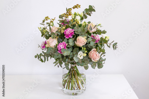 Ramo de rosas color champán, claveles y eucalipto en un jarrón de cristal sobre un fondo blanco.