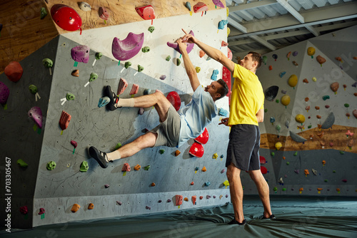 Male instructor teaching man to climb artificial wall. Man training, climbing up the artificial stones. Bouldering activity. Concept of sport, sport climbing, hobby, active lifestyle, school, course