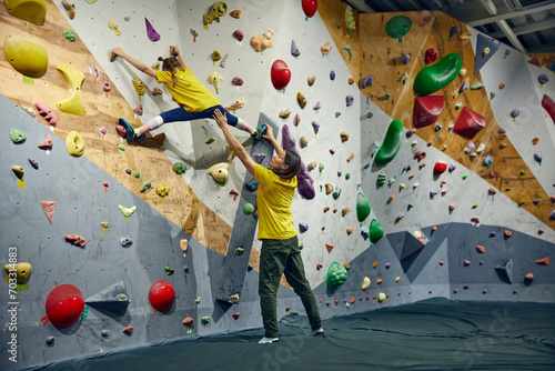Female bouldering trainer teaching little girl, child bouldering activity, techniques. Little girl climbing wall, indoor class. Concept of sport climbing, hobby, active lifestyle, school, course