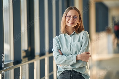 Smiling, standing with arms crossed, in glasses. Young woman in airport hall #703317296
