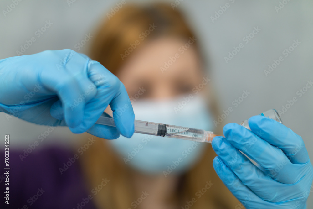 A close-up of a nurse's hands scooping clear liquid into a syringe. A close-up of a nurse's hands scooping clear liquid into a syringe.