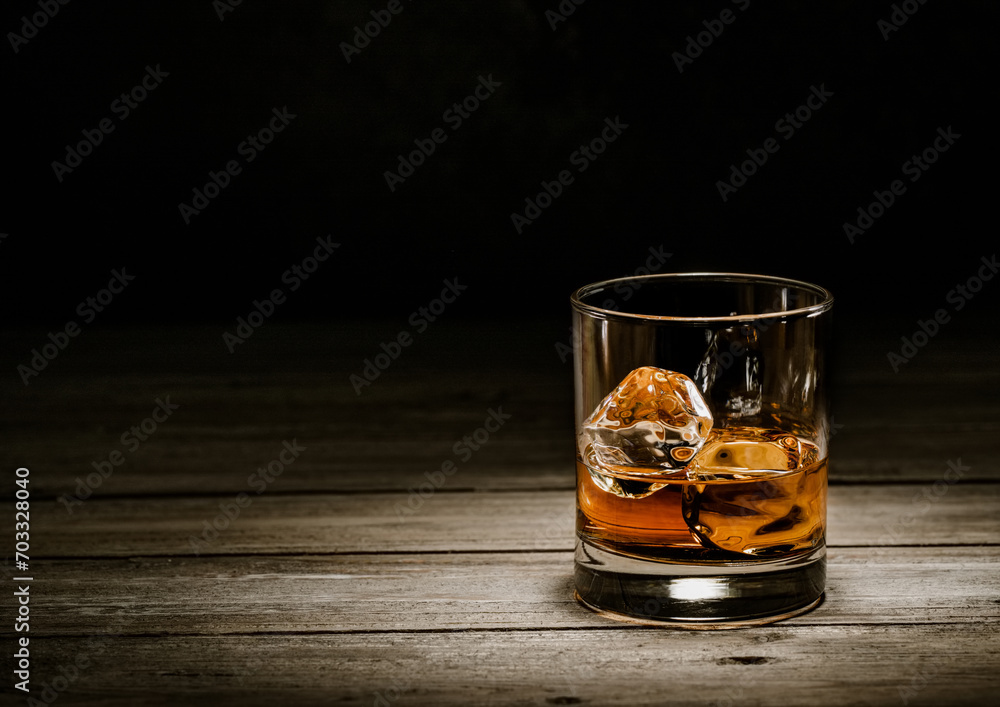Classic whiskey glass with ice cubes on wooden background.