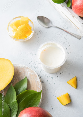 Fresh greek style yogurt with mango pieces and fresh fruits on light kitchen board.