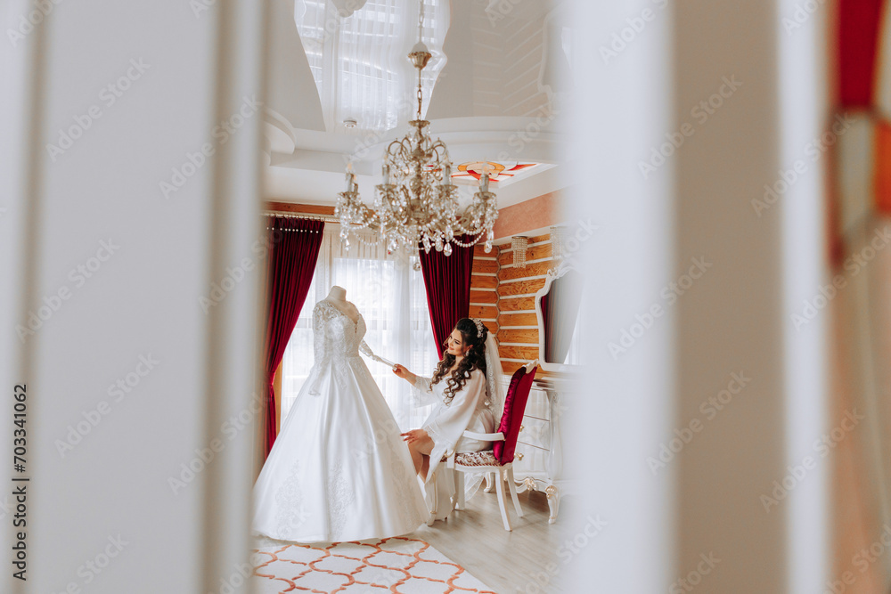 A happy bride is preparing for her luxurious wedding in a hotel room, with a wedding dress on a mannequin nearby. Portrait of a woman with fashionable hair, makeup and a smile in a dressing gown. A happy bride is preparing for her luxurious wedding in a hotel room, with a wedding dress on a mannequin nearby. Portrait of a woman with fashionable hair, makeup and a smile in a dressing gown.