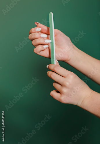 Crop woman filing long nails on green backdrop