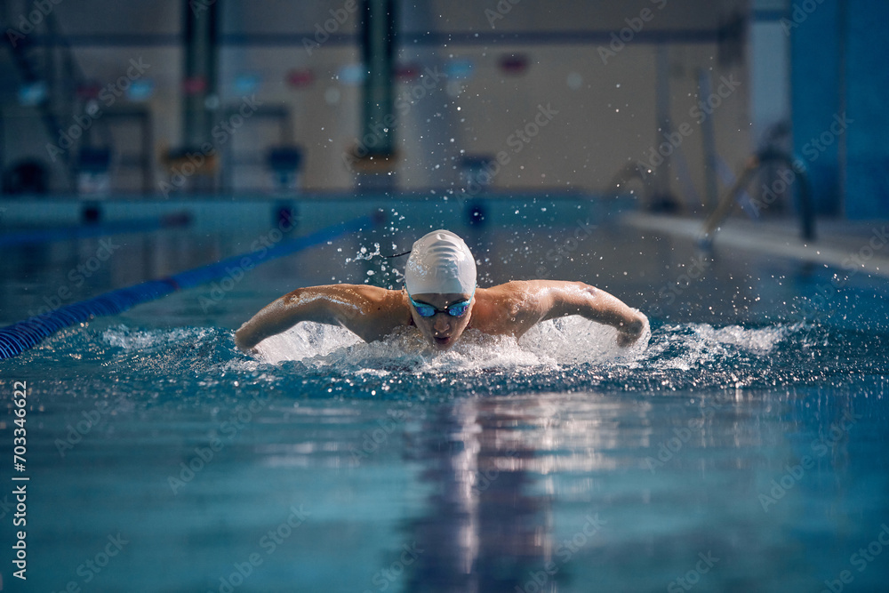 Butterfly swimming techniques. Athletic young man in motion, training, swimming in pool, wearing cap and goggles. Concept of pool sports, water sport, competition, active lifestyle