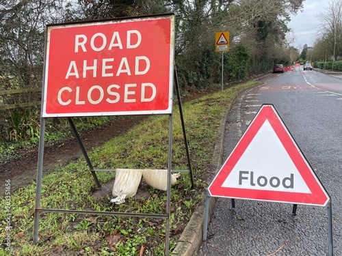 Two British road signs. Flood and road ahead closed. Standing in a road, cloudy weather, car on the background