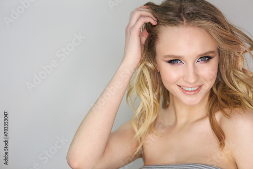 Young beautiful woman with blonde curly hair on grey background