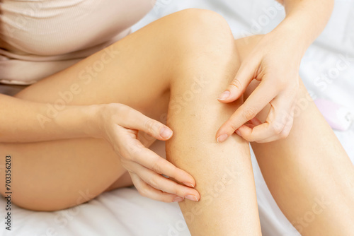 Young Caucasian woman touches her hairy legs with her hands. The female sits at home on a bed. Hair removal, depilation procedures for beauty. Naturalness, skincare, body care concept.