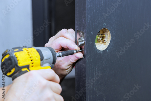 Installing lock handles with screwdriver on room door by carpenter