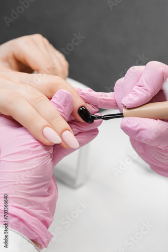 The manicurist covers the nails with black nail polish. Manicurist doing gel nails for a client.