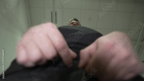 a young man with a beard and a hoodie and jeans appears in front of the camera and begins to unbuckle his belt and prepare to pee. shooting from the bottom point. A man in the toilet. photo